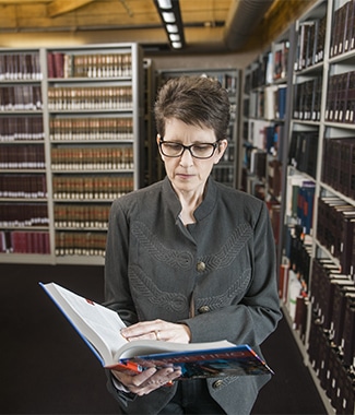 Female adult business student standing in library reading an open textbook