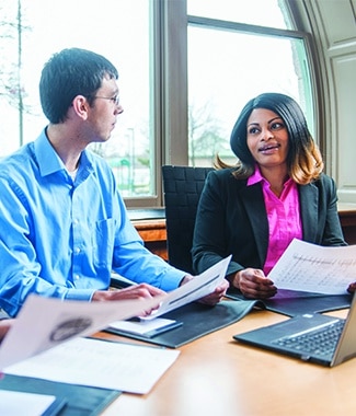 Female and male graduate students collaborating at a table with papers in front