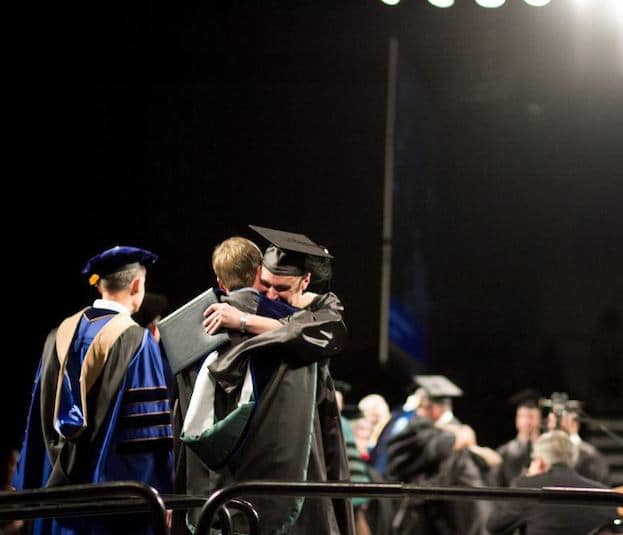 Male graduate student embracing an instructor during a commencement ceremony at Cornerstone University