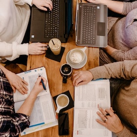 Overhead four adult students of gender diversity with open textbooks and laptops at a coffee shop in Grand Rapids, Michigan