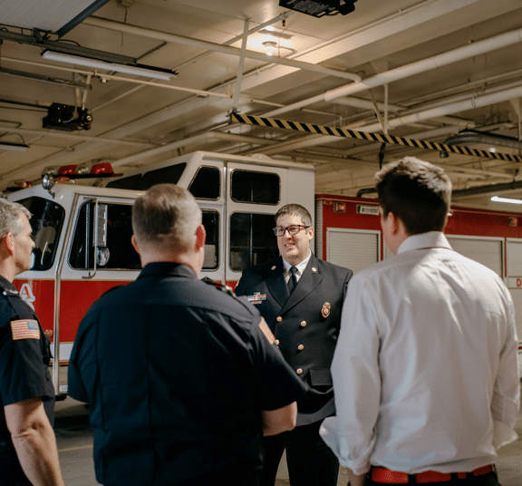 Male leader in uniform talking to three employees in fire department garage
