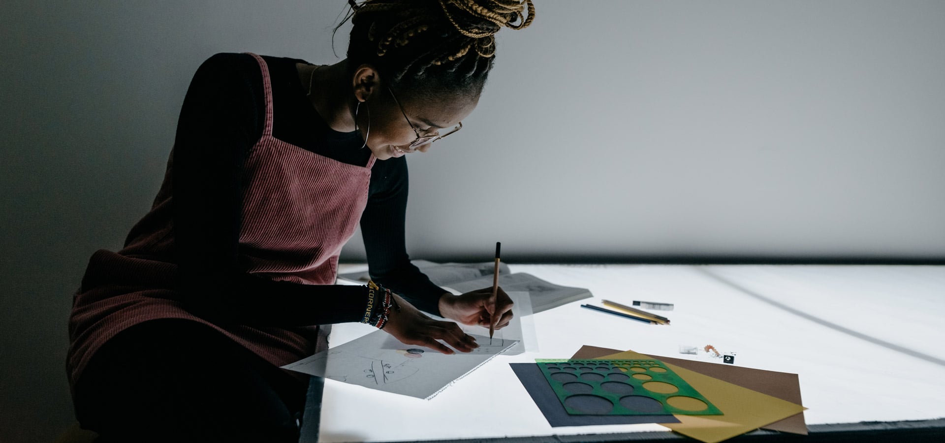 Female graphic design student using a light table to trace on papers with an open book and stencils