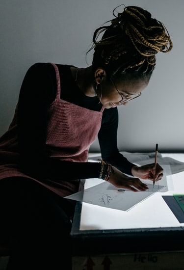 Female graphic design student using a light table to trace on papers with an open book and stencils