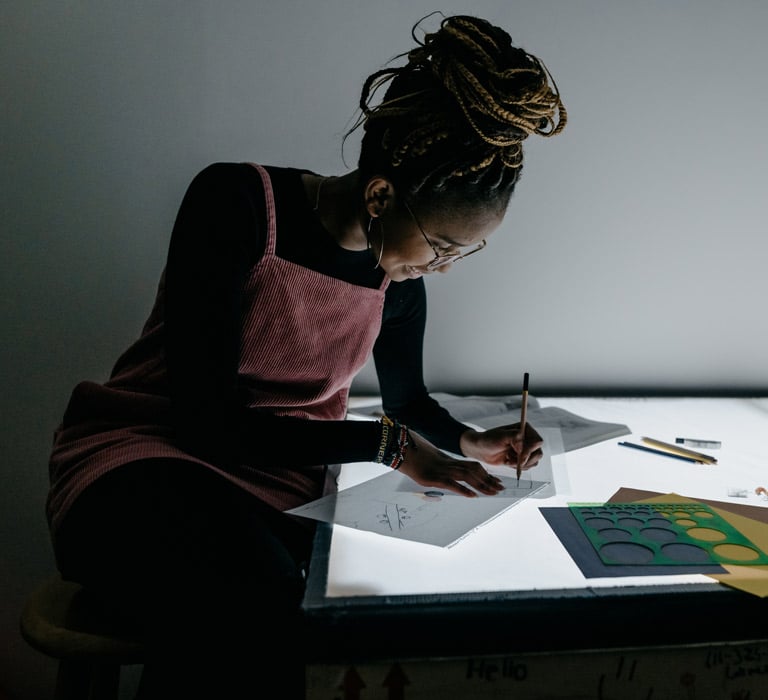 Female graphic design student using a light table to trace on papers with an open book and stencils