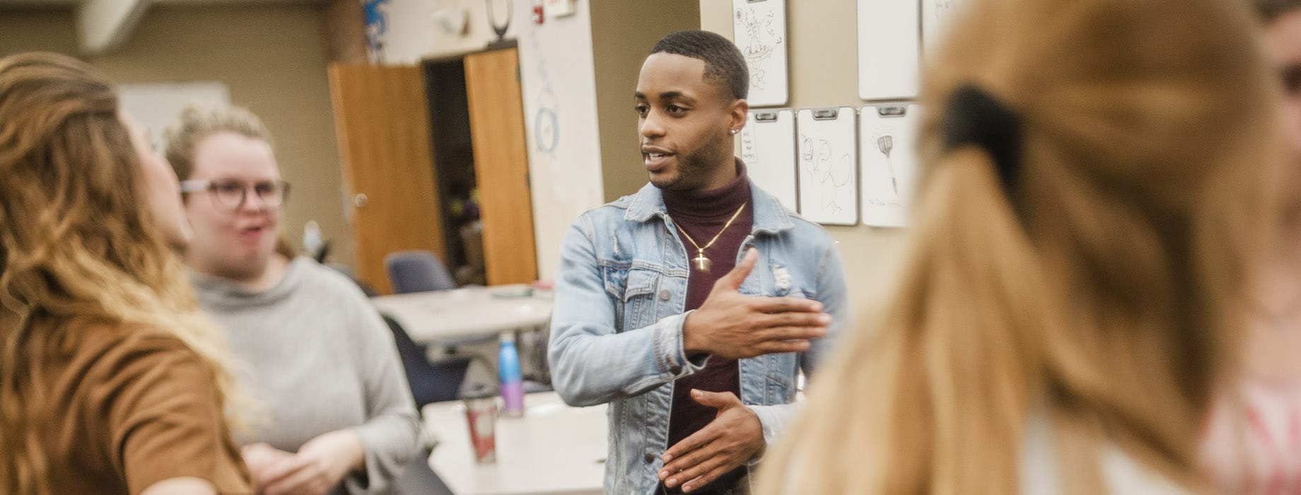 Male college student leading a group discussion with students while standing in a classroom
