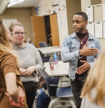 Male college student leading a group discussion with students while standing in a classroom