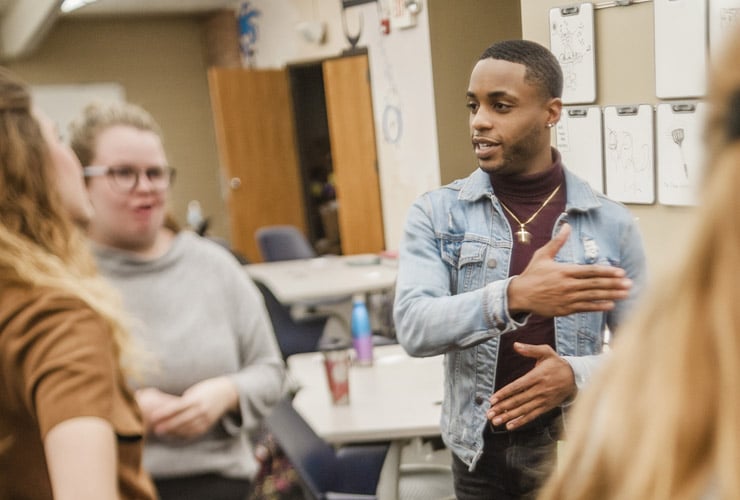 Male college student leading a group discussion with students while standing in a classroom
