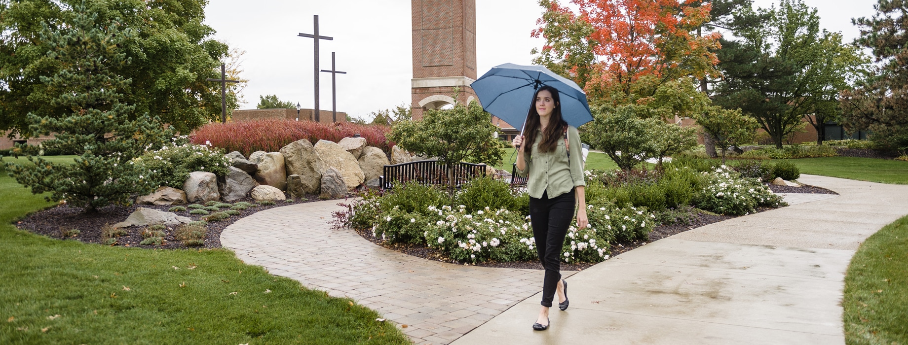 Female college student walking with an umbrella away from the bell tower on the campus of. Cornerstone University