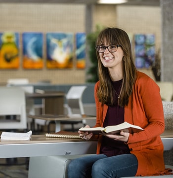 Female seminary student holding a Bible while sitting in the lobby of Grand Rapids Theological Seminary